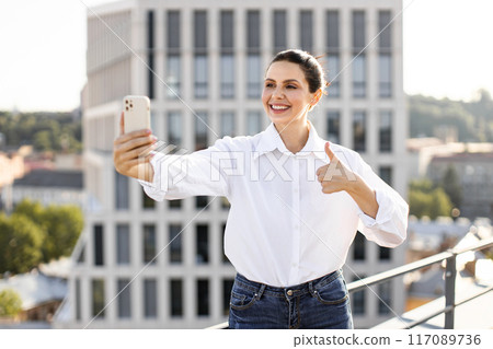 Smiling woman taking selfie on rooftop with thumbs up Smiling woman taking selfie on rooftop with thumbs up 117089736