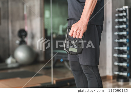 A man measuring his grip strength with a grip strength measuring device at a sports gym 117090185