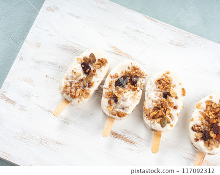 Homemade greek yogurt popsicles with granola on white wooden board 117092312