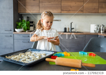 Little girl making cookie with dough using animal shape cutters in the home kitchen, Family concept Little girl making cookie with dough using animal shape cutters in the home kitchen, Family concept 117092319