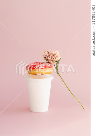 Donut with dried flower and paper coffee cup against pink background. Donut with dried flower and paper coffee cup against pink background. 117092402