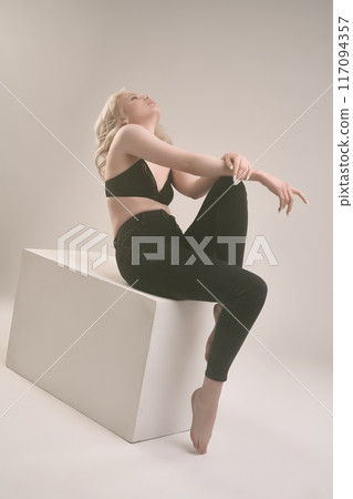 Sensual woman in tight clothing sitting on a white cube with reclining body 117094357