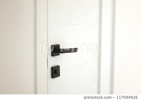 Minimalist white door with black handle and lock against a clean wall, perfect for modern interior design, architectural magazines, or home renovation projects 117094926