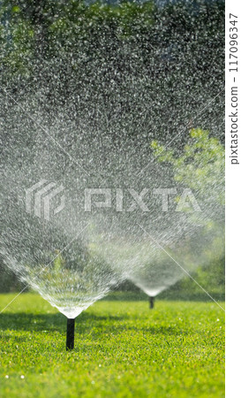 Multiple sprinklers watering a green lawn on a sunny day Multiple sprinklers watering a green lawn on a sunny day 117096347