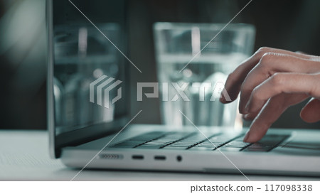 Female hands typing on computer close up. Woman user worker typing on laptop notebook keyboard desk working online with pc software apps. Drink water from glass, keep health balance hydration indoors Female hands typing on computer close up. Woman user worker typing on laptop notebook keyboard desk working online with pc software apps. Drink water from glass, keep health balance hydration indoors 117098338