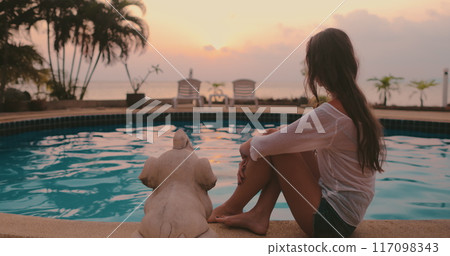 Long hair girl sit near swimming pool enjoy beautiful ocean sunset on tropical exotic island resort. Outdoor lifestyle travel summer holiday vacation. Relax, meditation, alone. Side view Long hair girl sit near swimming pool enjoy beautiful ocean sunset on tropical exotic island resort. Outdoor lifestyle travel summer holiday vacation. Relax, meditation, alone. Side view 117098343