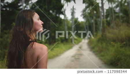 Beautiful long hair woman leisurely strolling jungle pam tree forest trail close up. Caucasian girl explore exotic island nature, relax, enjoy outdoor lifestyle travel on summer holiday vacation. Asia 117098344