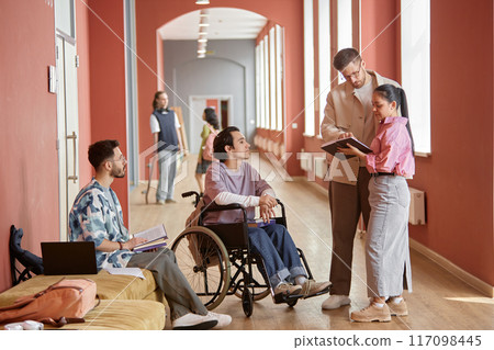 Diverse group of students asking adult male professor question during informal conversation in pink university hallway Diverse group of students asking adult male professor question during informal conversation in pink university hallway 117098445