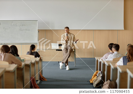 Wide angle shot of adult male teacher lecturing students on civil law speaking in hand held microphone in university classroom with whiteboard, copy space Wide angle shot of adult male teacher lecturing students on civil law speaking in hand held microphone in university classroom with whiteboard, copy space 117098455