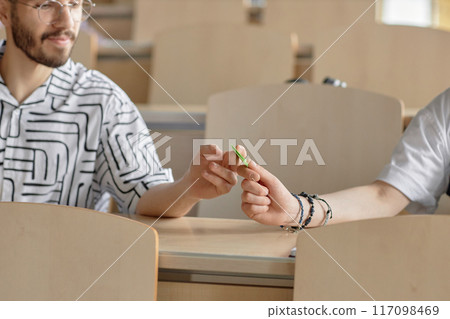 Cropped shot of male Middle Eastern student handing note to to his classmate while sitting at desk in university lecture hall, copy space Cropped shot of male Middle Eastern student handing note to to his classmate while sitting at desk in university lecture hall, copy space 117098469