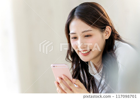 A woman watching a smartphone with a smile A woman watching a smartphone with a smile 117098701