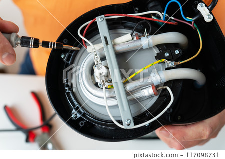 Close-up of hands repairing a speaker, intricate wiring and components visible. 117098731