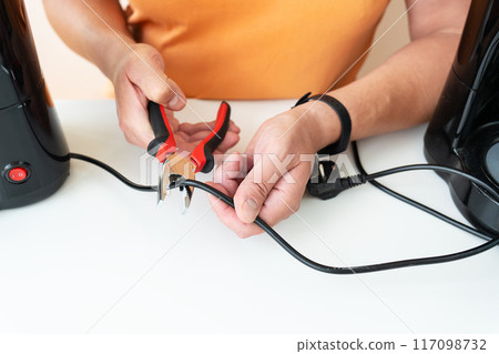 Hands using pliers to cut a black cable on a white background, highlighting manual work and electrical maintenance. 117098732