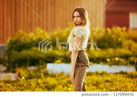 Beautiful slim white woman 26 years old, knee-length portrait in light of setting sun in summer in countryside. Beautiful slim white woman 26 years old, knee-length portrait in light of setting sun in summer in countryside. 117099456