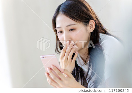 一個女人驚訝地看到一部智能手機 一個女人驚訝地看到一部智能手機 117100245