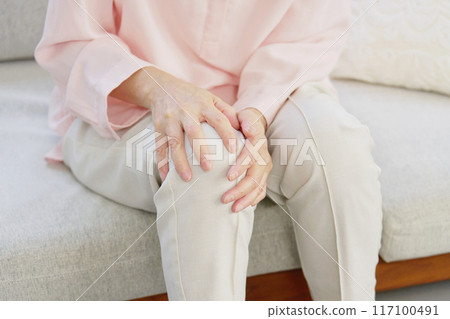 Senior woman with knee pain, living room, no face 117100491