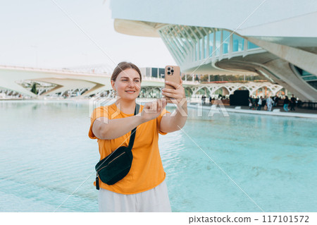 Young traveling woman taking selfie outdoors. Concept of travel, tourism and vacation in city. Ciudad de las Artes y las Ciencias de Valencia.Valencia City of Arts and Sciences. High quality photo 117101572