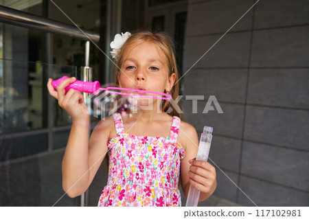 Young Girl Enjoying Bubble Blowing Activity on a Sunny Day Outside 117102981