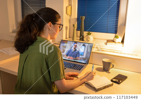 Rear view of young woman working at laptop. Remote work from home and online calling. Remote consultation with psychologist. Concept of modern freelancing and education 117103449