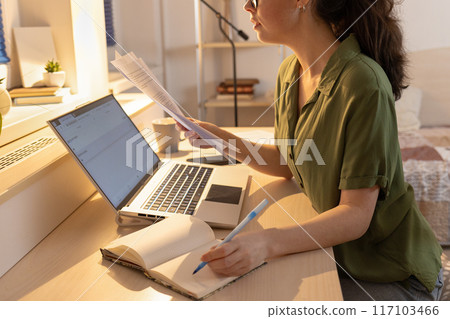 Side view of young woman working at laptop. Remote work from home and online consultation with psychologist. Concept of modern freelancing and education Side view of young woman working at laptop. Remote work from home and online consultation with psychologist. Concept of modern freelancing and education 117103466