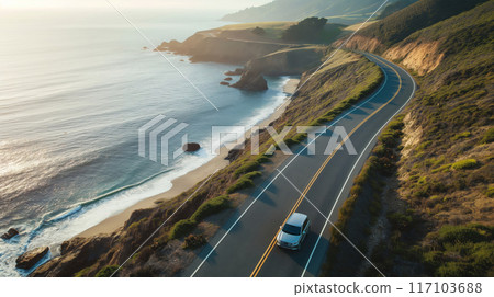 Aerial view of a car driving along a scenic coastal highway during golden hour 117103688