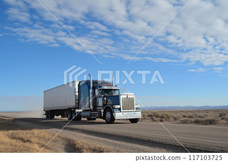 Semi truck drives on a highway with a clear blue sky in a desert setting 117103725