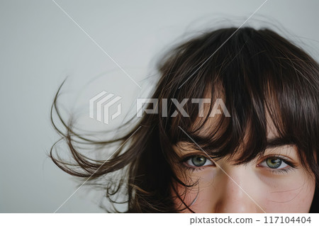 Close-up image focusing on a woman's eyes peering through her fashionable, tousled bangs 117104404