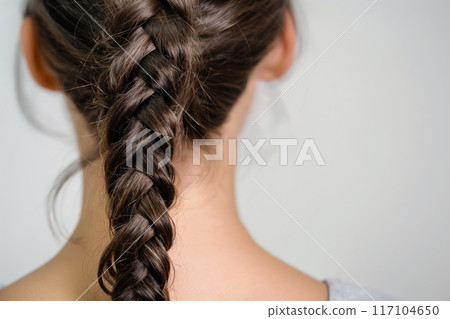 Close-up image of a woman featuring a detailed fishtail braid against a neutral background 117104650