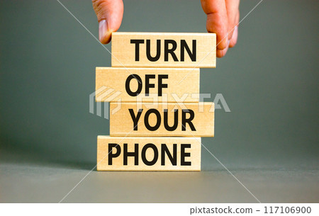 Turn off your phone symbol. Concept words Turn off your phone on wooden blocks. Beautiful grey table grey background. Businessman hand. Business psychological turn off your phone concept. Copy space 117106900