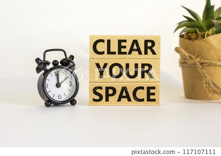 Clear your space symbol. Wooden blocks with words 'Clear your space'. Beautiful white background, black alarm clock, house plant. Business, clear your space concept, copy space. 117107111