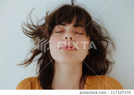 Serene woman with a playful, messy fringe hairstyle photographed against a neutral background 117107276