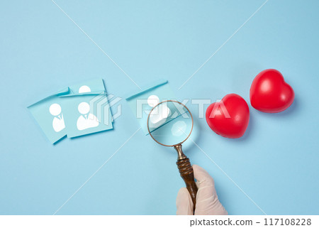 Female hand holding magnifying glass and red hearts on blue background, donor selection 117108228