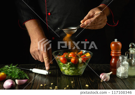 Adding paprika to chopped vegetables in a bowl. Chef preparing a salad of fresh vegetables and spices. Vegetable diet concept for a hotel Adding paprika to chopped vegetables in a bowl. Chef preparing a salad of fresh vegetables and spices. Vegetable diet concept for a hotel 117108346