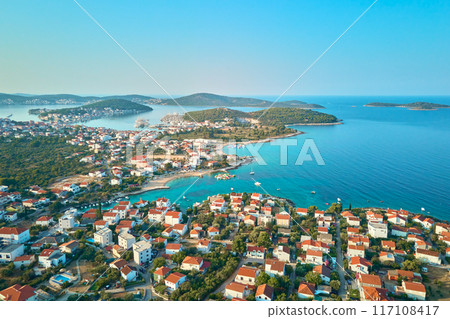 Aerial view of coastal town with colorful buildings near sea coastline. Touristic city for summer vacation with red roof houses and Islands in Adriatic sea. Panoramic view of Rogoznica town in Croatia Aerial view of coastal town with colorful buildings near sea coastline. Touristic city for summer vacation with red roof houses and Islands in Adriatic sea. Panoramic view of Rogoznica town in Croatia 117108417