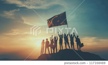 Silhouetted entrepreneurs on top of a mountain, victoriously raising a flag at sunset 117108489