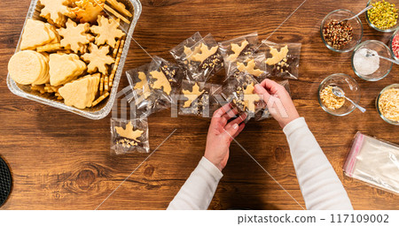 Carefully packaging Christmas cutout cookies, half-dipped in chocolate, sprinkled with crushed nuts, and presented in clear cellophane wrapping. 117109002