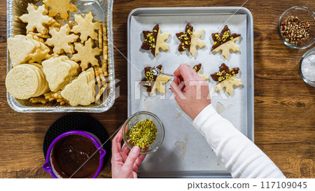 Flat lay. Creating snowflake-shaped cutout sugar cookies, dipped in chocolate, and adorned with different toppings. 117109045