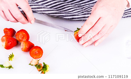 Succulent red strawberries, some showing early spoilage, are arrayed on a white cutting board, held securely in place, with a paper towel lined glass bowl nearby suggesting an attempt at preservation. 117109119