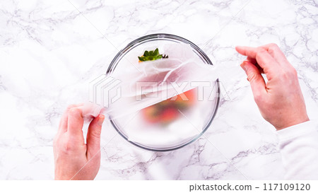 Flat lay. Strawberries, freshly washed and dried, are neatly stored in a glass bowl lined with a paper towel and securely covered with plastic wrap to maintain freshness. 117109120