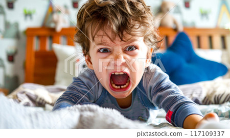 Little boy with his mouth wide open on bed with stuffed animal. AI 117109337