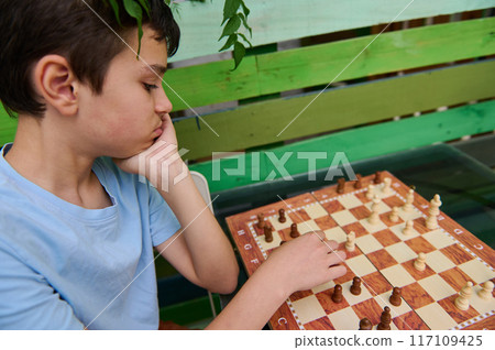 Young boy contemplating his next move in a game of chess outdoors 117109425