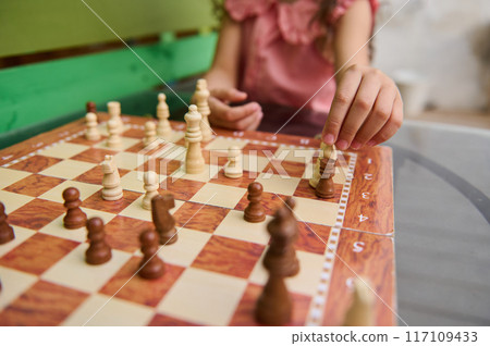 Close-up of child playing chess outdoors on a sunny day Close-up of child playing chess outdoors on a sunny day 117109433