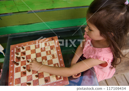Young girl playing chess outdoors, focusing intently on the game 117109434