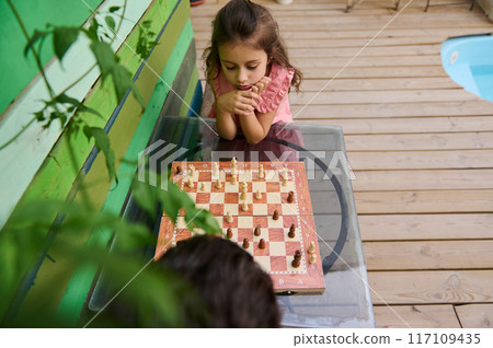 Little girl concentrating on a chess game outdoors Little girl concentrating on a chess game outdoors 117109435