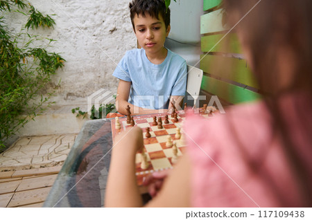 Children playing chess outdoors, focusing on strategy and concentration 117109438