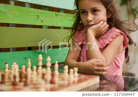 Thoughtful girl contemplating a chess move outdoors in summer 117109447