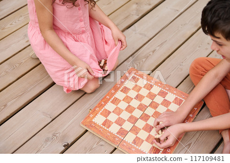 Children playing chess on a wooden deck during a sunny day outdoors 117109481