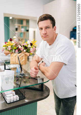 Vertical portrait of serious muscular male standing waiting at counter of modern dentistry clinic, looking at camera. Front view of confident young man customer in shopping mall 117109900