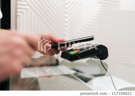 Closeup side view of purchase by smartphone on electronic payment machine or card reader. Closeup of unrecognizable male customer cashless payment apply smartphone to card reader machine, slow motion. Closeup side view of purchase by smartphone on electronic payment machine or card reader. Closeup of unrecognizable male customer cashless payment apply smartphone to card reader machine, slow motion. 117109922