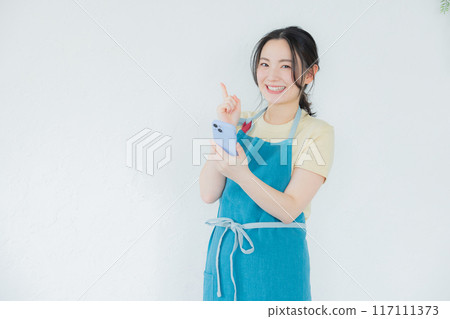 A woman in an apron looking at her smartphone A woman in an apron looking at her smartphone 117111373